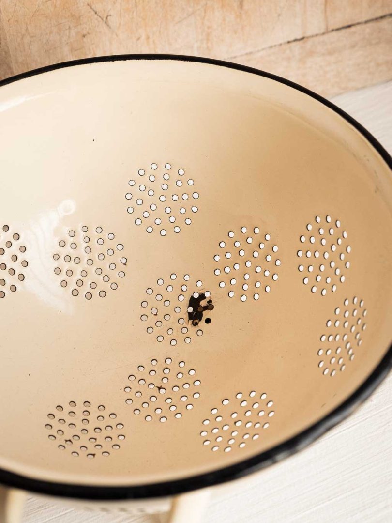 Passoire vintage en métal émaillé beige et motifs rouge, détail oxydation